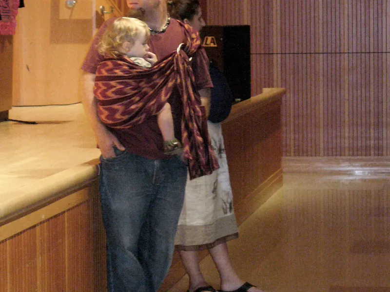 Father carrying a toddler in a patterned ring sling