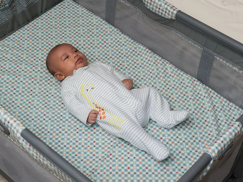 Baby lying in a travel cot wearing a sleepsuit