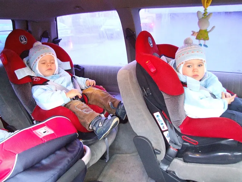 Two babies strapped into rear car seats on the back seat