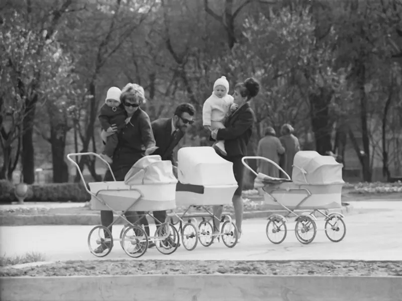 Parents with three classic prams on an evening walk in the park