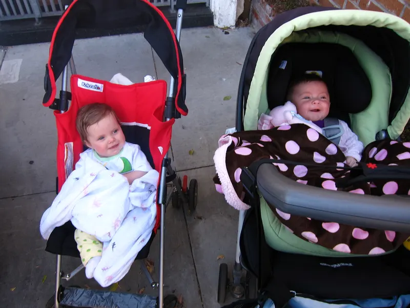 Two babies tucked into modern prams outdoors