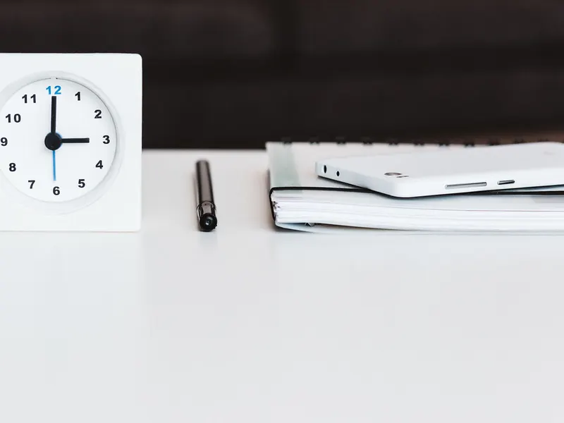 Clock, pen and notebook on a tidy white desk