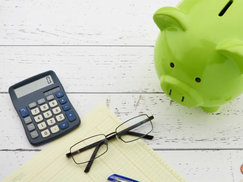 Piggy bank, calculator and glasses on a table