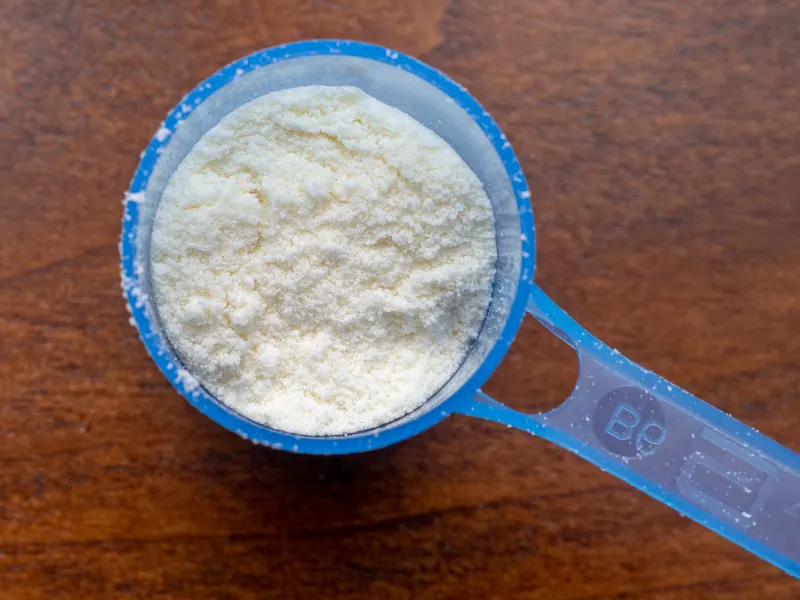Scoop of powdered infant formula in a blue measuring spoon