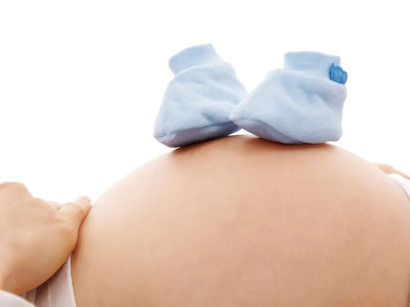 Knitted blue baby booties resting on a pregnant bump