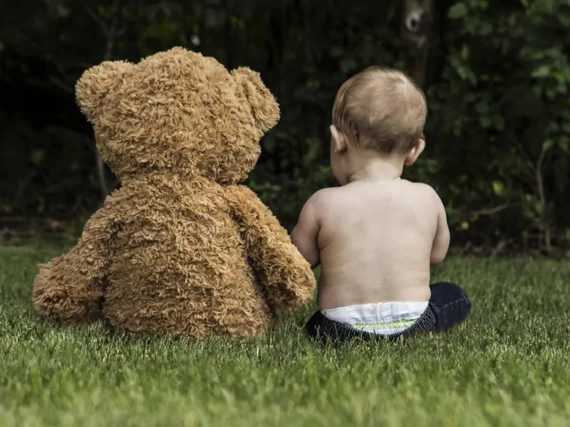 Toddler sitting on the grass beside a big teddy bear