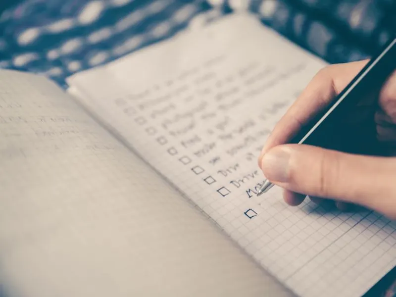 Hand ticking items off a handwritten checklist in a notebook