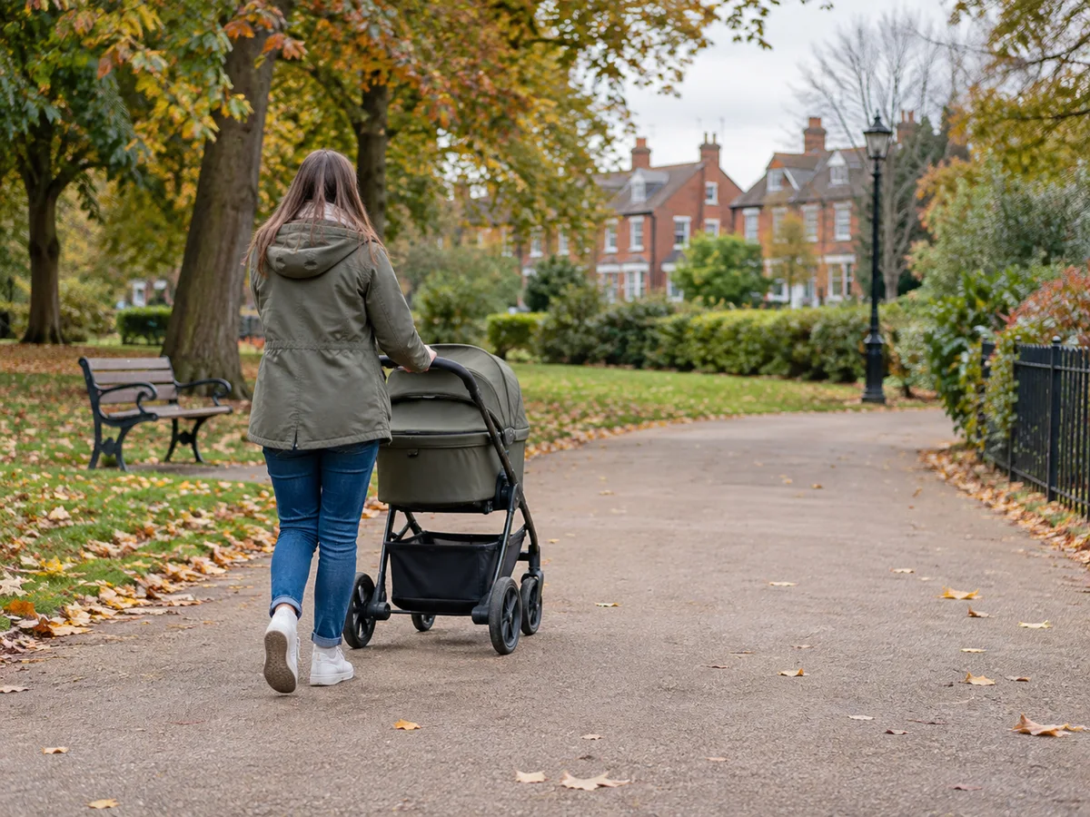 Parent pushing a modern pushchair along a leafy British park path