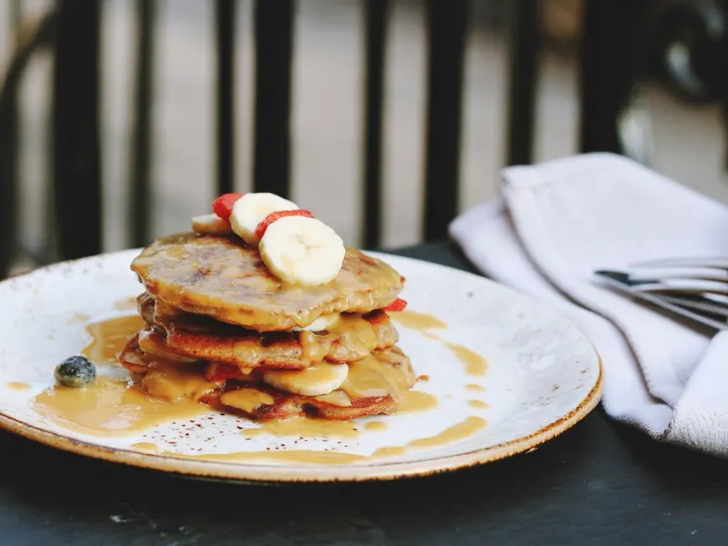 Stack of pancakes topped with banana slices and syrup