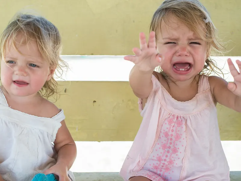 Upset toddler crying next to a sibling